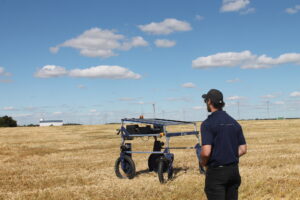 Remote operator standing in field with R-Tech Rover